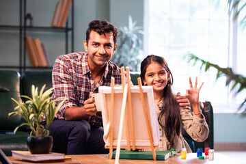 Indian daughter painting on easel, father encouraging her, family bonding indoors