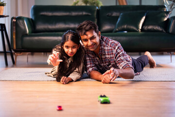 Indian father and daughter playing toy car race, sharing quality playful time at home