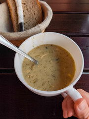 Warm bowl of creamy soup with spoon and bread basket on wooden table in cozy autumn setting