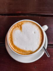 Coffee cup with heart-shaped foam on wooden table, perfect for autumn October ambiance