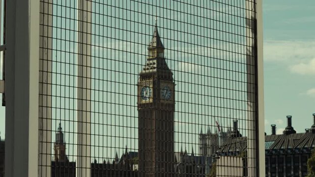 Big Ben clock tower viewed through a metal grid fence, geometric pattern overlays historic city skyline under blue sky.