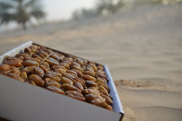 A box of fresh dates placed on the sand in the Tunisian desert, capturing the natural beauty of local agriculture and traditional date harvesting in North Africa.