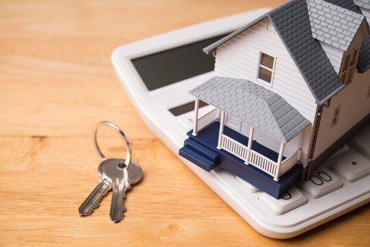 House model on white calculator and house key on wooden table background. Homebuyers, mortgage loan, banking, real estate investment trust (REIT), reverse mortgage, home selling or rental concept.