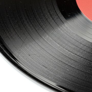 Close up of a black vinyl record with a bright red label showing detailed grooves and reflections on a clean white background highlighting the