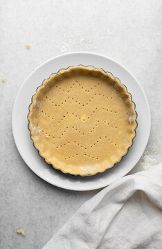Overhead view of a frozen tart shell in a a tart tin, raw tart pastry crust on white marble countertop, process of making tart
