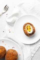 Overhead view of fried scotch eggs on white plate, top view of cross-section of scotch eggs on white dish