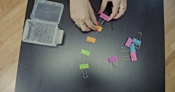 A close-up view of hands meticulously connecting colorful binder clips, forming a long chain. The video features crisp and satisfying sounds, perfect for ASMR content or office-related projects.