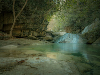 Beautiful tropical waterfall flowing into turquoise lagoon surrounded by lush green forest, peaceful nature landscape with crystal clear water, rocks and sunlight reflections in jungle