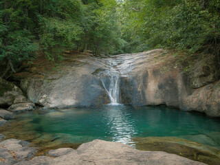 Beautiful tropical waterfall flowing into turquoise lagoon surrounded by lush green forest, peaceful nature landscape with crystal clear water, rocks and sunlight reflections in jungle