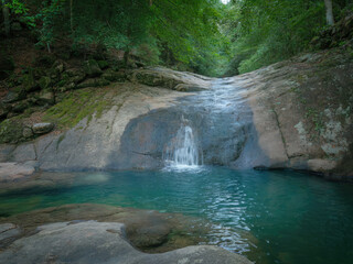 Beautiful tropical waterfall flowing into turquoise lagoon surrounded by lush green forest, peaceful nature landscape with crystal clear water, rocks and sunlight reflections in jungle