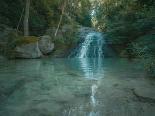 Beautiful tropical waterfall flowing into turquoise lagoon surrounded by lush green forest, peaceful nature landscape with crystal clear water, rocks and sunlight reflections in jungle