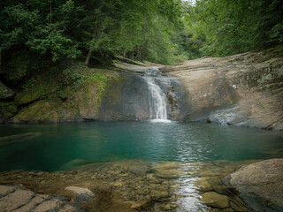 Beautiful tropical waterfall flowing into turquoise lagoon surrounded by lush green forest, peaceful nature landscape with crystal clear water, rocks and sunlight reflections in jungle