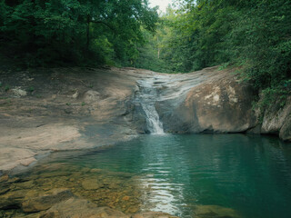 Beautiful tropical waterfall flowing into turquoise lagoon surrounded by lush green forest, peaceful nature landscape with crystal clear water, rocks and sunlight reflections in jungle