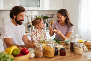 A family of three shares happy moments in their kitchen, preparing snacks. The parents and child engage in fun activities, creating joyful memories together.