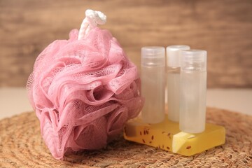 Pink shower puff, soap and cosmetic products on wicker mat, closeup