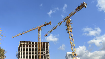 Urban construction site with tower cranes and high rise building against blue sky