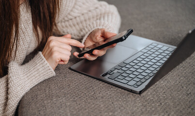 Focused woman uses her smartphone while sitting at a laptop, engaged in business communication or chatting.
