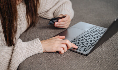 Woman's hand holds a credit or debit bank card while typing on a laptop for a secure online purchase