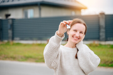 Happy woman holds a set of keys on a fob with a new house or apartment in the background after a successful closing