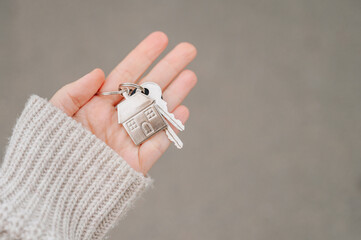 Close-up of a person's hand holding a metal keychain with house keys and a fob against a blurred background