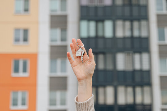Close-up of a person's hand holding a metal keychain with house keys and a fob against a blurred background