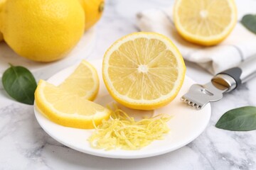 Lemon zest, fresh fruits, zester tool and green leaves on light marble table, closeup