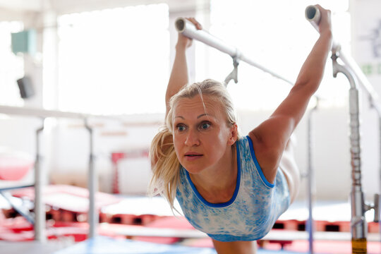 Woman gymnast performs complex acrobatic exercise on parallel bars in gym - Powered by Adobe