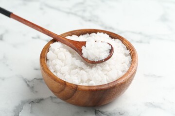 Sea salt in bowl and spoon on white marble table, closeup