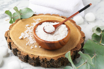 Sea salt in bowl, spoon, towels and eucalyptus leaves on white marble table, closeup