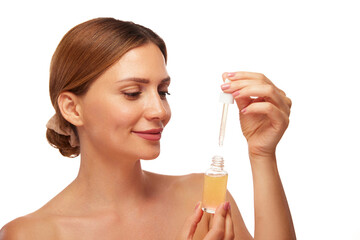Fototapeta premium A young woman with glowing skin carefully uses a dropper to apply a facial serum in a simple, bright environment. Her smile shows joy and excitement about skincare.