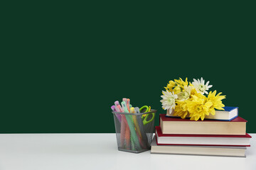 Happy teacher's day. Flowers, books and stationery on white table against chalkboard. Space for text