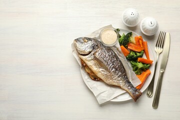 Salt, pepper shakers, tasty roasted dorado fish, vegetables, sauce and cutlery on light wooden table, flat lay. Space for text