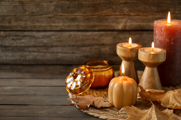 Autumn atmosphere. Many different burning candles and dry leaves on wooden table, closeup. Space for text