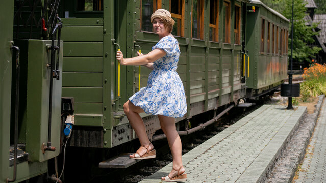 Cheerful woman in vintage sundress boards a nostalgic steam train, evoking Summer Weaving Festival's charm and wanderlust nostalgia