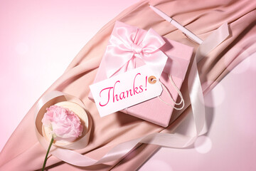 Thank you card design with gift box and flower on pink background, top view. Bokeh lights
