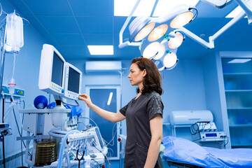 Doctor using medical equipment in operating room. A female doctor adjusting monitoring equipment in a modern operating room.