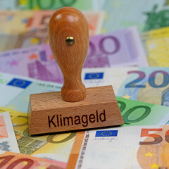 Stempel mit dem Aufdruck "Klimageld" vor Geldscheinen