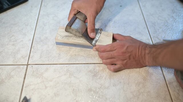 Close-up of a person sharpening an axe blade on a whetstone, careful hand work during metal honing process on tiled floor