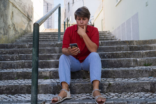 Sad woman sitting on stairs with a phone. no signal, no money, or afraid to call her boyfriend