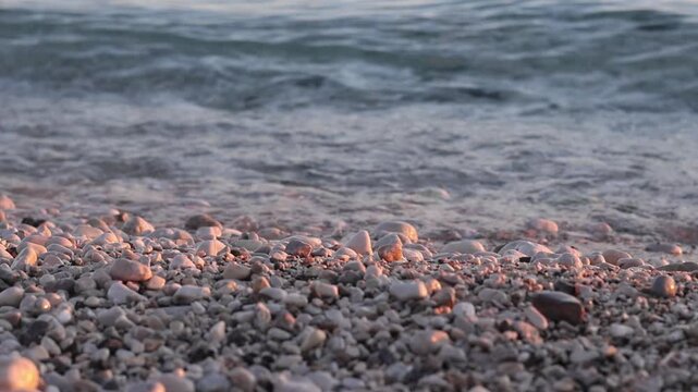 Smooth pebbles and stones at the beach as gentle waves reflect the warm glow of sunset. Golden hour seascape, coastal shoreline in soft sunlight. Scenic view capturing the peaceful beauty of nature