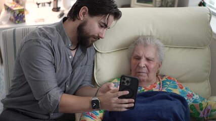 Grandson delights in showing heartfelt memories to his grandmother on his smartphone. Their laughter fills the cozy living room filled with love and connection. - Powered by Adobe