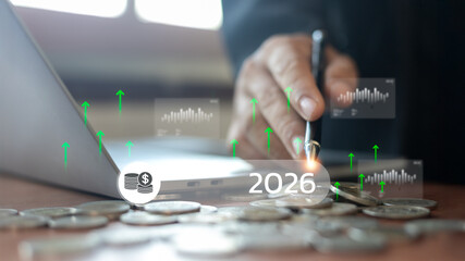 Future financial growth concept for the year 2026 showing coins, a laptop, and handwriting with upward arrows, representing investment planning, business success, and economic forecast.