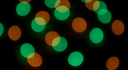 Abstract background with blurred green and orange bokeh lights creating a festive and dreamy atmosphere for holiday or party designs