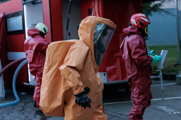Emergency responders in orange and red chemical protection hazmat suits and full face masks...