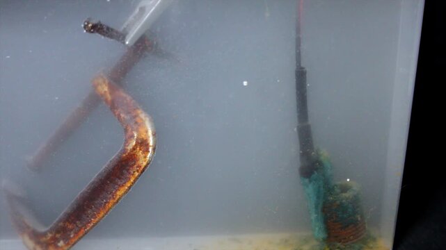 Electrolytic reduction tank with negative electric charge on c-clamp to clean rust off it.