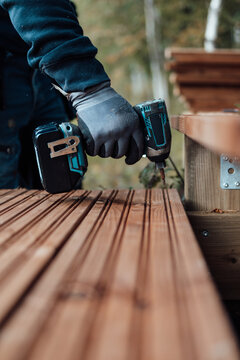 Carpenter using cordless drill on wooden deck outdoors