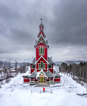 Aerial view of the striking red and white Buksnes Church stands proudly amidst a pristine blanket of snow, Gravdal, Nordland, Norway.