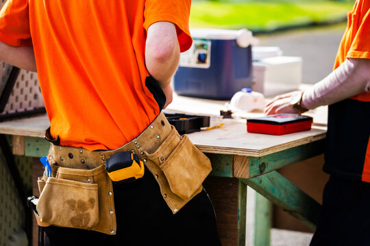 trade apprentice wearing tool belt working at wooden bench outdoors