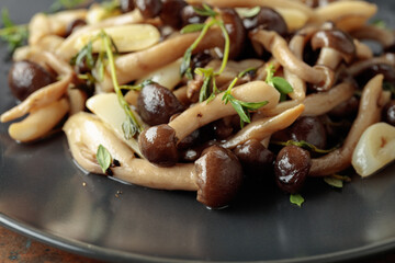 Fried shimeji mushrooms with thyme and garlic on a black plate.