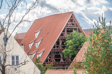 Historisches renovierungsbedürftiges Gerberhaus mit Fachwerk, Dachgauben und Sprossenfenstern vor dramatischem Wolkenhimmel und grünem Baum im Gerberviertel in Nördlingen.